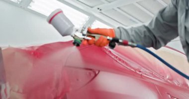 Bir araba boyacısı, bir otomotiv dükkanındaki kırmızı tamponu tamir ediyor ve boyuyor. Bir haznede sprey tabanca kullanıyor. Otomotiv boyama servisi. Araba Boyacısı Oto Servisi 'nde Kırmızı Tampon Tamiri