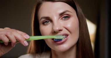 Diş teli takan, dişlerini yeşil diş fırçasıyla fırçalayan genç bir kadın. Diş hijyen rutinine yakın çekim, ağız bakımını ve ortodontik tedaviyi teşvik. Sağlıklı gülümseme kavramı.
