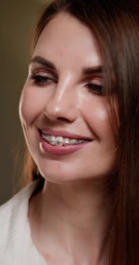Dikey video. Diş teli tutan, diş fırçası kullanan, ağız hijyeni ve ortodontik sağlığı destekleyen genç bir kadın. Yakın çekim, diş sağlığı rutinine odaklanarak olumlu ifadeyi yakalar. Diş ParçalarıComment