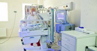 Yenidoğan bakımı ve hastane hizmeti kavramı. Prematüre bebek hastane kuvözünde tıbbi bakım görüyor. Eldivenli ve tıbbi ekipmanlı bebek üzerinde çalışan tıbbi personel.