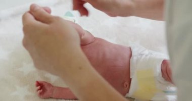 Sıcak elli ve yumuşak dokunuşlu yumuşak bebek masajı. Eller nazikçe yeni doğan ellere masaj yapıyor rahatlatıcı ve rahatlatıcı bir atmosfer yaratıyor. Bebek yumuşak masasında bere ve bebek bezi takıyor. Nazik bebek