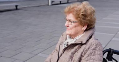 Açık hava ortamında, tekerlekli sandalyede oturan yaşlı bir kadın neşeli bir şekilde gülümsüyor ve gününün tadını çıkarıyor. Tekerlekli sandalyedeki yaşlı bir kadın Güzel Günışığında dışarıda eğleniyor.