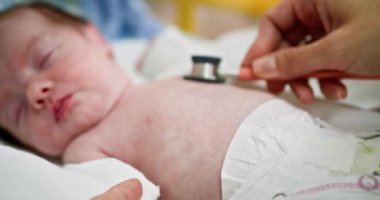 Bir sağlık uzmanı yeni doğmuş bir bebeği hastane ortamında steteskop kullanarak değerlendirir. Yenidoğan ünitesinde yeni doğanlar için kapsamlı bir sağlık kontrolü yapılması gereklidir.
