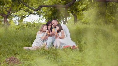 Renkli pipetlerden cam şişede meyve suyu içen iki tatlı kızı olan beyaz anne ve babaların portresi. Gülümseyen aile doğaya keyifle vakit geçiriyor. İki kızı olan ebeveynler içki içiyor.