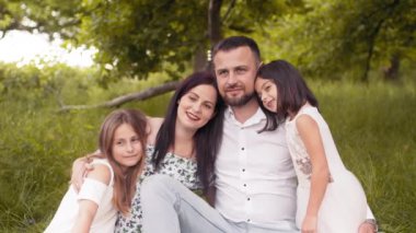 Beautiful caucasian family enjoying summer picnic at green garden. Father, mother and two daughters sitting in hugs on soft blanket. Concept of togetherness and love. Parents with two daughters.