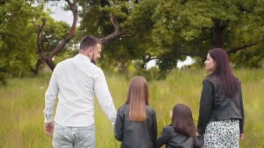 Çekici hamile anne ve babamın yeşil bahçede yürüyen iki küçük kızıyla el ele tutuşması. Genç bir kadın yaz günlerini çocuklarla temiz hava alarak geçiriyor. İki kızı olan ebeveynler..