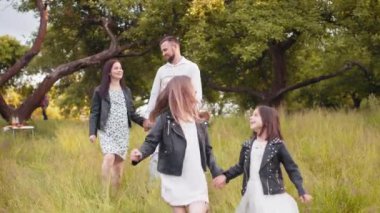 İki çocuklu pozitif aile yaz günlerini yeşil bahçede geçiriyor. Genç ebeveynler yürür ve arkada konuşurlar. Dört kişilik mutlu bir aile temiz havanın tadını çıkarıyor. İki çocuklu aile.