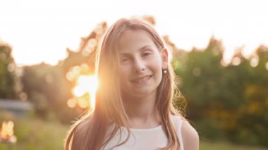 Beautiful blond young girl with freckles outdoors looking, hair blowing in wind on nature background, close up portrait, slow motion. Little girl in park. Lonely girl in green field