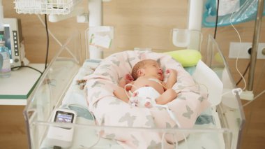 Newborn baby resting in a hospital incubator. The infant is being monitored and receiving medical care. Represents neonatal intensive care. clipart