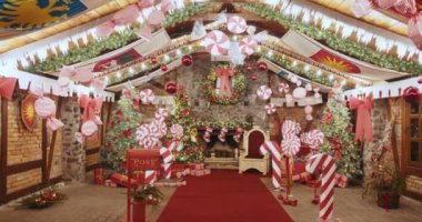 Noel Baba 'nın büyülü evinde canlı dekorasyonlarla dolu şenlikli bir Noel sahnesi. Madalyalı ağaçlar, baston şekerler, çelenkler neşeli bir tatil ruhu yaratır. Tatil kutlamaları için tasarlanmış kapalı mekanlar.