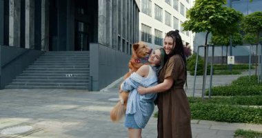 İki yetişkin kadın, biri uzun örgülü, diğeri günlük giysiler içinde, şehir ortamında dost canlısı köpekleri okşuyor. Kızı ve annesi birlikte vakit geçiriyorlar..