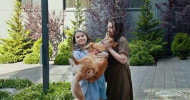 Beyaz anne ve genç kız evcil köpekleri ile dışarıda kaliteli zaman geçiriyorlar. Anne köpeği nazikçe öperken kız onu mutlu bir şekilde tutar. Sahne, sevgi ve aile bağlarını taşır.