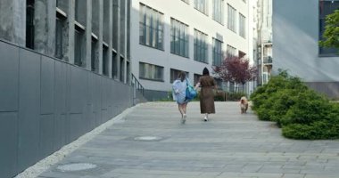 Kızı ve annesi birlikte vakit geçiriyorlar. İki genç kadın, Asyalı ve Kafkasyalı, modern şehir caddesinde yeşillik içinde yürüyen köpek. Şehir arkadaşlığı ve hayvan bakımı kavramı.