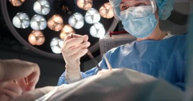 Modern cerrahi odasında parlak ışıklar altında ameliyat yapan beyaz kadın cerrah. Prosedür sırasında hasta bakımı ve güvenliğini sağlamak için hassas operasyonlar yapan tıp uzmanları.