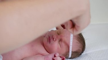 Klinik ortamında yeni doğmuş bir bebeğin kafa çevresini ölçen bir doktor. Bebeğe tıbbi bakım yapılıyor gibi görünüyor, muhtemelen yeni doğan fototerapisi..