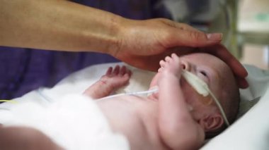 Yenidoğan yoğun bakım ünitesindeki bir bebekle ilgileniliyor. Elleri nazikçe başının üstünde dinleniyor ve bakım ve endişeyi vurguluyor..