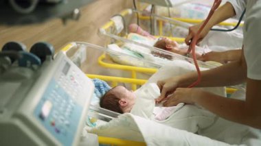 Yeni doğan bir bebeği beşiğinde diğer bebeklerle birlikte yenidoğan yoğun bakım ünitesinde muayene eden bir sağlık görevlisi..