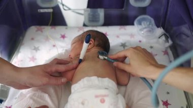 Bir doktor steteskoplu yeni doğmuş bir bebeği muayene eder, hastane ortamında tıbbi bakım ve yenidoğan sağlık hizmetleri sunar..