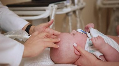 Doktor, küçük bir bebeğe kafatası ultrasonu yapar ve bebeğin kafasını tıbbi bir ortamda muayene eder. Bebeklerin kafasının ultrason taraması. Çocuklarda erken tıbbi teşhis için ultrason kullanımı