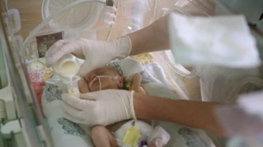 Prematüre bir bebek yoğun bakımda sütle besleniyor, yenidoğan bakımı ve erken beslenme vurgulanıyor. Prematüre bir bebek yenidoğan yoğun bakım ünitesinde süt alır.