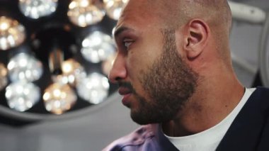 Koruyucu giysiler içindeki koyu tenli doktor, ameliyat lambalarıyla aydınlık ameliyathanede gözlerini kaçırıyor. Endişeli, endişeli doktor ameliyattan önce ya da sonra, genç cerrah