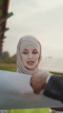 A woman wearing a hijab reviews documents near solar panels, likely related to renewable energy.