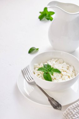 Beyaz arka planda beyaz bir fincanda granüllerde taze süzme peynir.