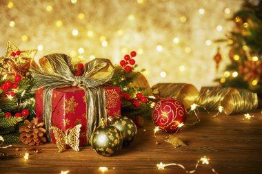 Lambalardan bir çelenk ile Noel kompozisyonu. Noel ağacı dalları, kırmızı hediye kutusu toplar, külahlar ve ahşap bir masanın üzerindeki altın dekor.