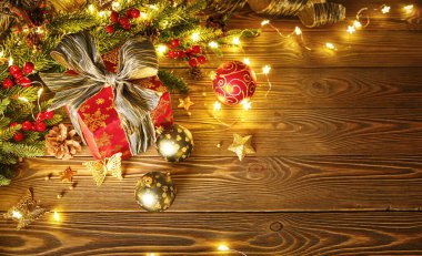 Lambalardan bir çelenk ile Noel kompozisyonu. Noel ağacı dalları, kırmızı hediye kutusu toplar, külahlar ve ahşap bir masanın üzerindeki altın dekor.
