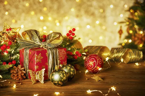 Lambalardan bir çelenk ile Noel kompozisyonu. Noel ağacı dalları, kırmızı hediye kutusu toplar, külahlar ve ahşap bir masanın üzerindeki altın dekor.