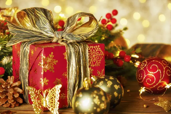 Lambalardan bir çelenk ile Noel kompozisyonu. Noel ağacı dalları, kırmızı hediye kutusu toplar, külahlar ve ahşap bir masanın üzerindeki altın dekor.