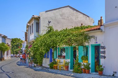 Bozcaada, Türkiye, 17 Temmuz 2024, eski güzel evleri ve parlak çiçekleri olan renkli sokaklar, adanın caddelerinde yürüyen turistler