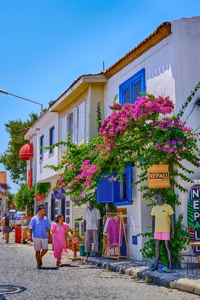 Bozcaada, Türkiye, 17 Temmuz 2024, eski güzel evleri ve parlak çiçekleri olan renkli sokaklar, adanın caddelerinde yürüyen turistler