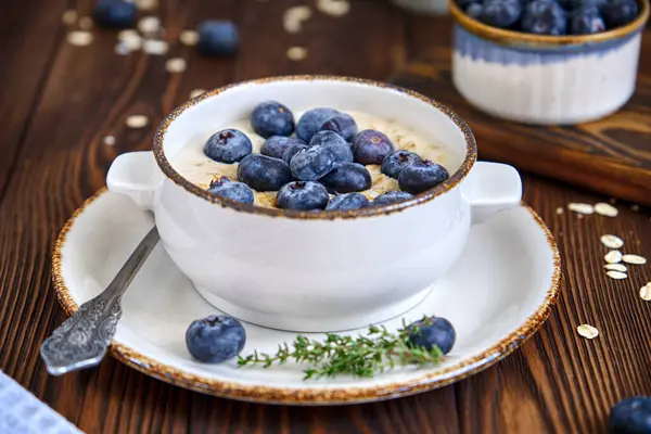 Sütlü ve yaban mersinli yulaf ezmesi ve eski ahşap bir masada bir fincan sade kahve.