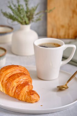 Beyaz tabakta çıtır çıtır kruvasan ve gri arka planda bir fincan sade kahve. Lezzetli ve sağlıklı kahvaltı.