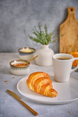 Beyaz tabakta çıtır çıtır kruvasan ve gri arka planda bir fincan sade kahve. Lezzetli ve sağlıklı kahvaltı.