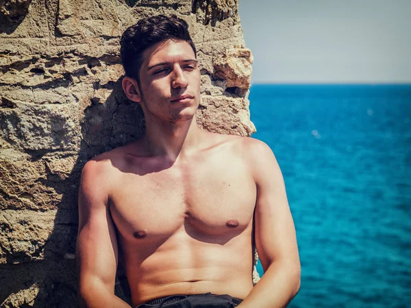 Komea Nuori Mies Istuu Meren Rannalla Paidattomana Aurinkoisena Päivänä — kuvapankkivalokuva