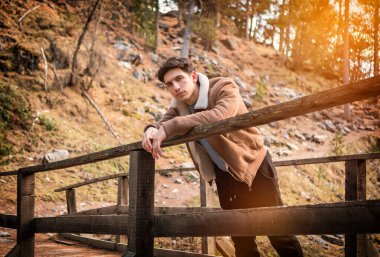 Sonbaharda ya da kışın dağlarda çekici bir genç adam, soğuk hava, süet ceket giymiş, kameraya bakıyor.