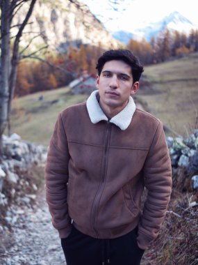 Sonbaharda ya da kışın dağlarda çekici bir genç adam, soğuk hava, süet ceket giymiş, kameraya bakıyor.