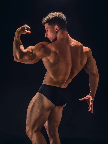 若い筋肉の男性のボディビルダーは ブリーフでポーズ スタジオで黒の背景を撮影 — ストック写真
