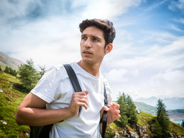 Przystojny Młodzieniec Spacerujący Plecakiem Bujnej Zielonej Scenerii Górskiej Odwracając Wzrok — Zdjęcie stockowe
