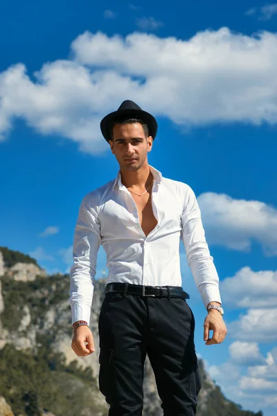 エレガントな白いシャツと黒フェドーラの帽子で若いハンサムな男 屋外ながら カメラを見て 後ろの青い空 — ストック写真