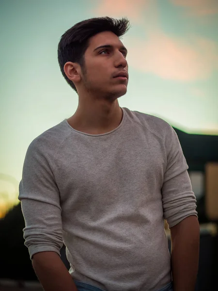 Handsome young man in white sweater outdoor in street, looking at camera
