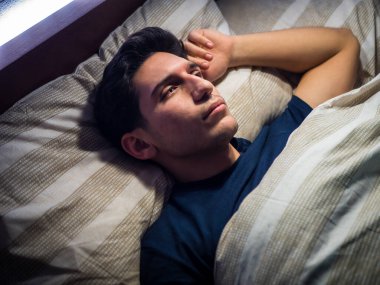 Çekici genç adam yatakta uzanıyor, düşünüyor, yukarı bakıyor.