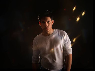 Stüdyonun arka planında, tişörtlü, kameraya bakan yakışıklı genç adamın yarı vücut görüntüsü.