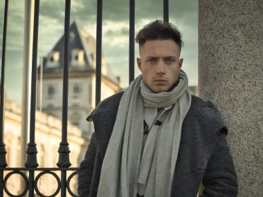 Avrupa 'nın kentsel ortamında yakışıklı bir genç kış günü siyah ceket ve eşarp giyip metal kapıya yaslanıyor.