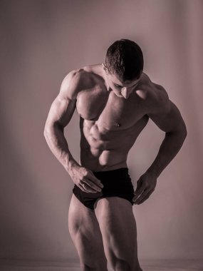 Stüdyodaki yakışıklı erkek vücut geliştirici, dramatik ışıklandırmayla, külot giyiyor.,