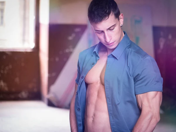 Attractive young man opening shirt to show muscular body, wearing jeans and shirt on naked torso