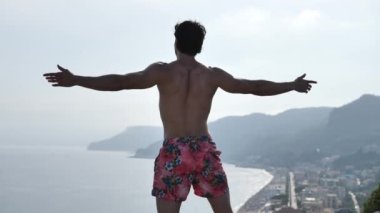 Genç adam gömleksiz, kollarını açmış, açık denizde özgürlüğün tadını çıkarıyor, arkadan görülüyor..