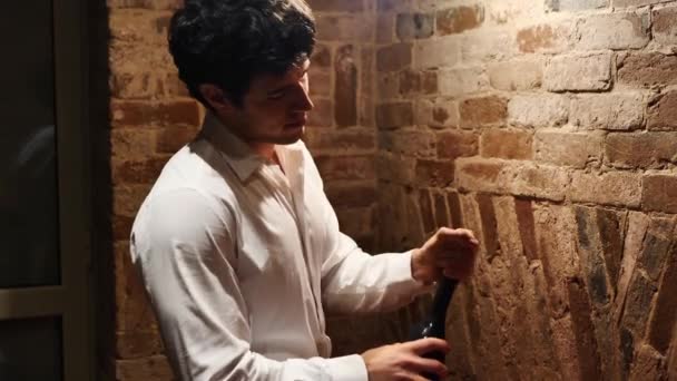 年轻迷人的男人打开香槟酒瓶 拔掉瓶塞 穿上典雅的白衬衫 — 图库视频影像
